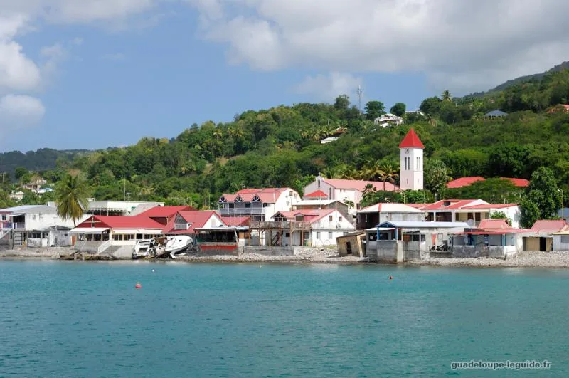 Le bourg de Deshaies vu depuis la mer : maisons aux toits rouges, église et pontons de pêcheurs au pied du morne