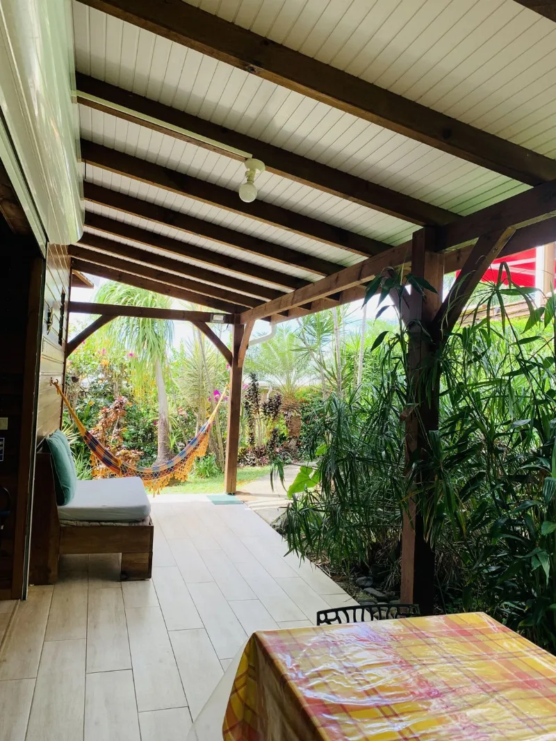 Terrasse couverte d'un cottage, hamac tendu devant le jardin tropical et banquette en bois
