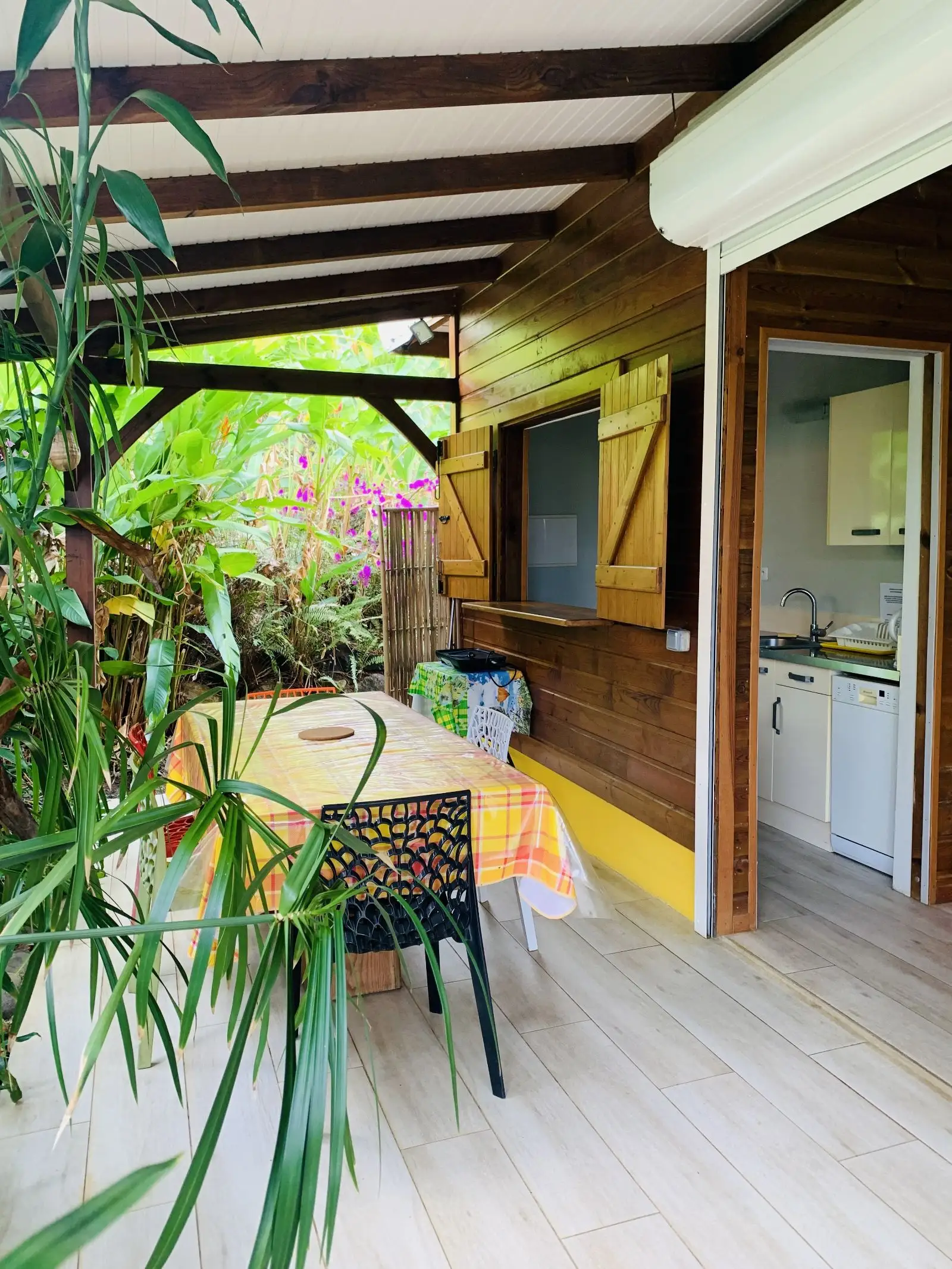 Terrasse couverte en bois avec table nappée de madras, ouverte sur le jardin tropical