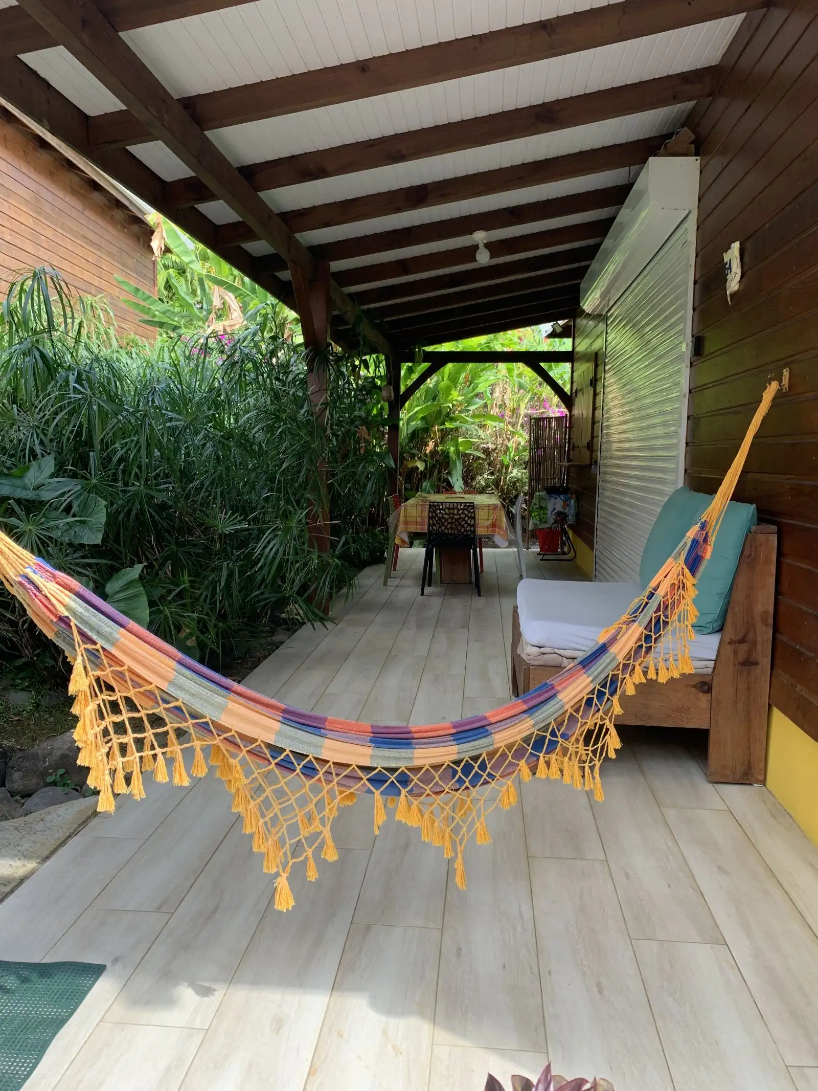 Hamac coloré tendu en travers de la terrasse, devant la banquette et la table de repas