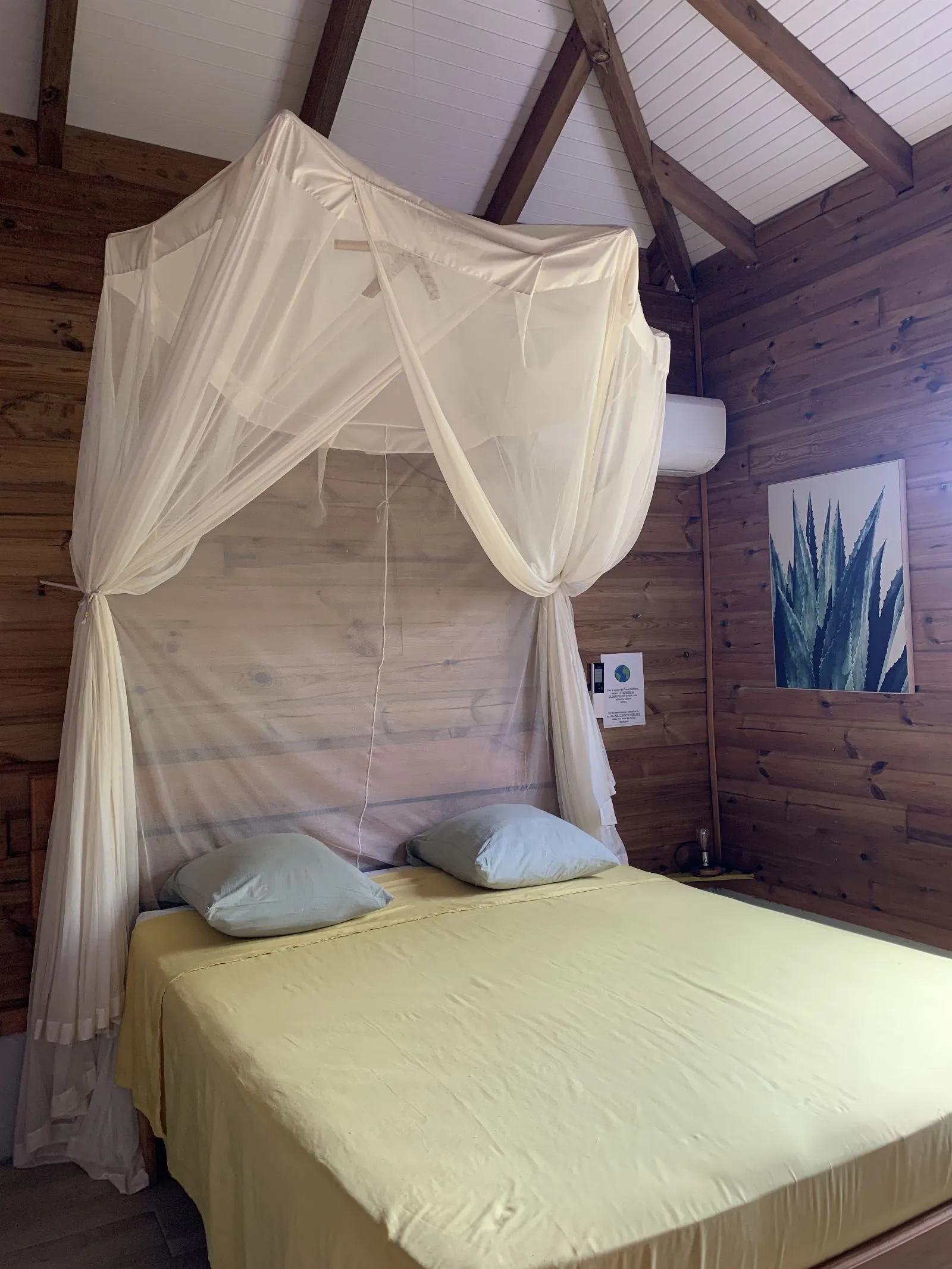 Lit double sous moustiquaire à baldaquin, dans une chambre lambrissée sous charpente
