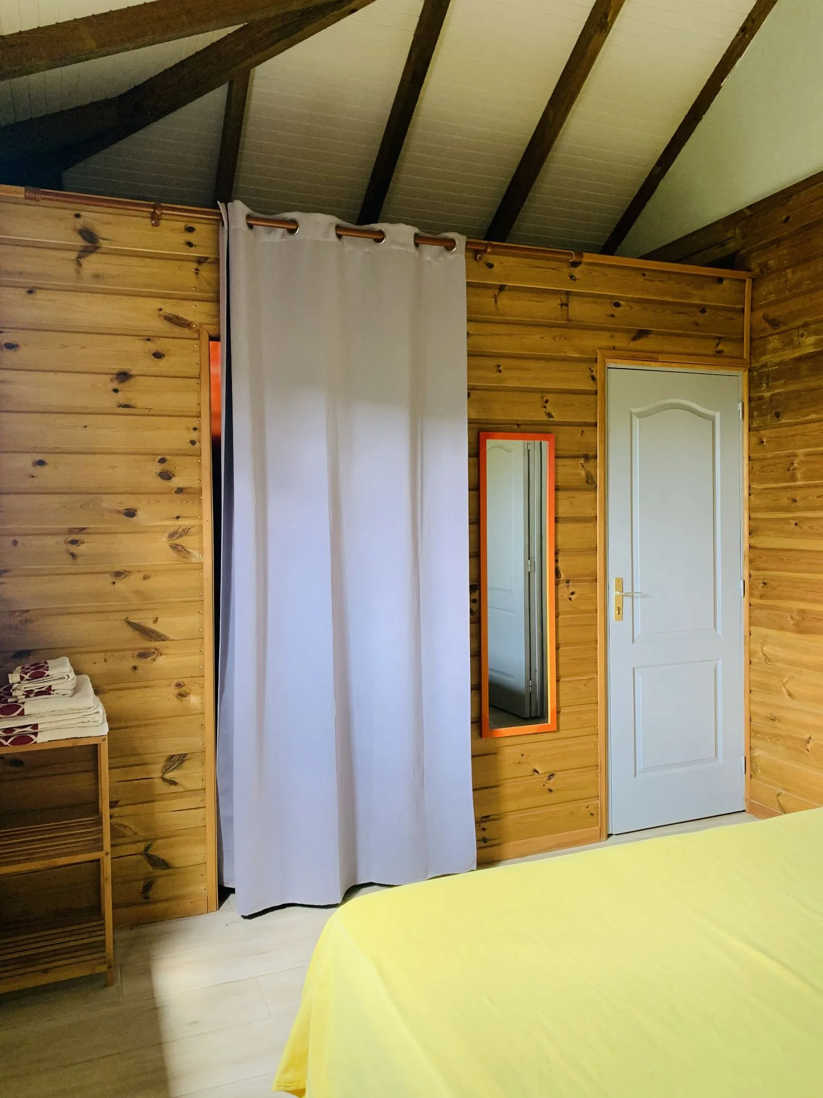Chambre lambrissée avec rideau, miroir et porte de la salle d’eau
