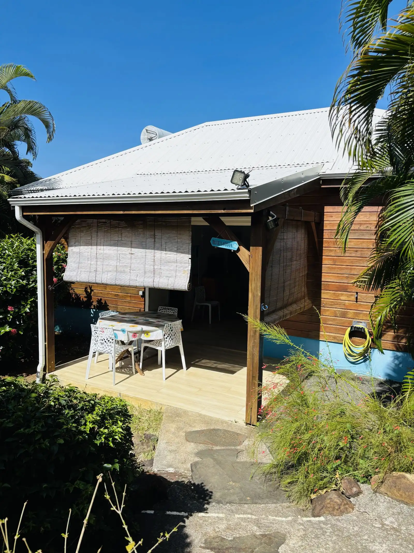 La façade d’un cottage en bois sous un toit de tôle, avec sa terrasse couverte et sa table dressée