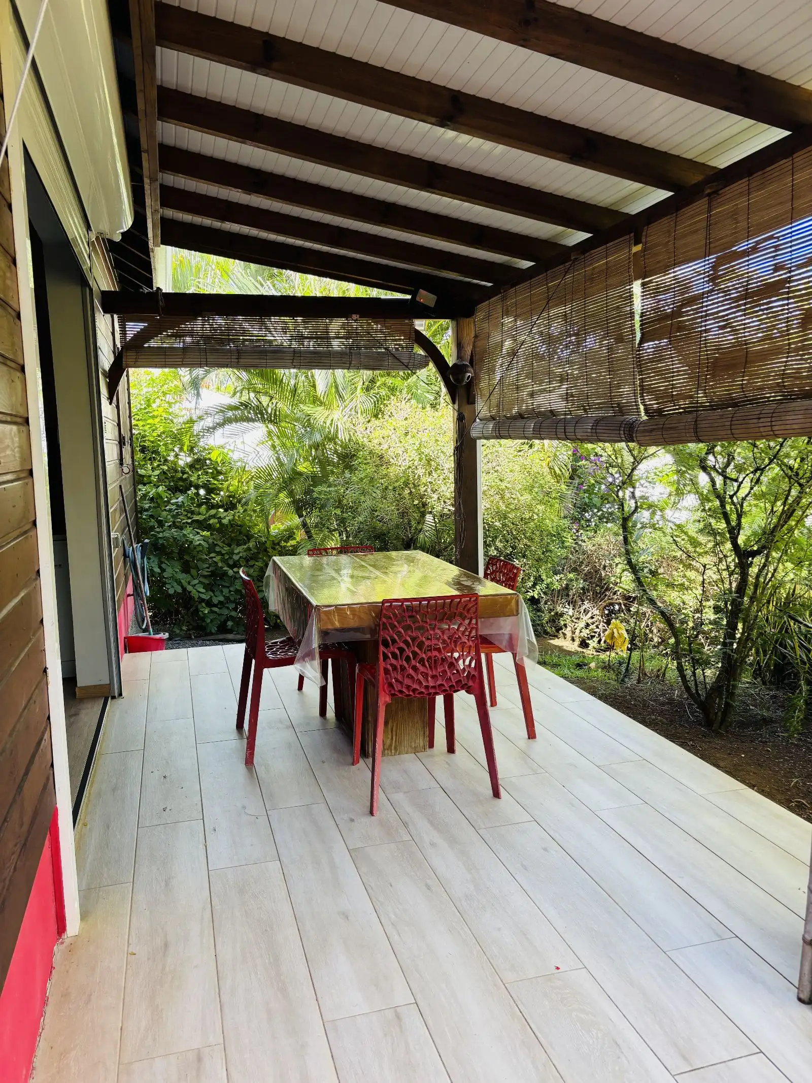 Terrasse couverte en bois avec table et chaises rouges, ouverte sur le jardin