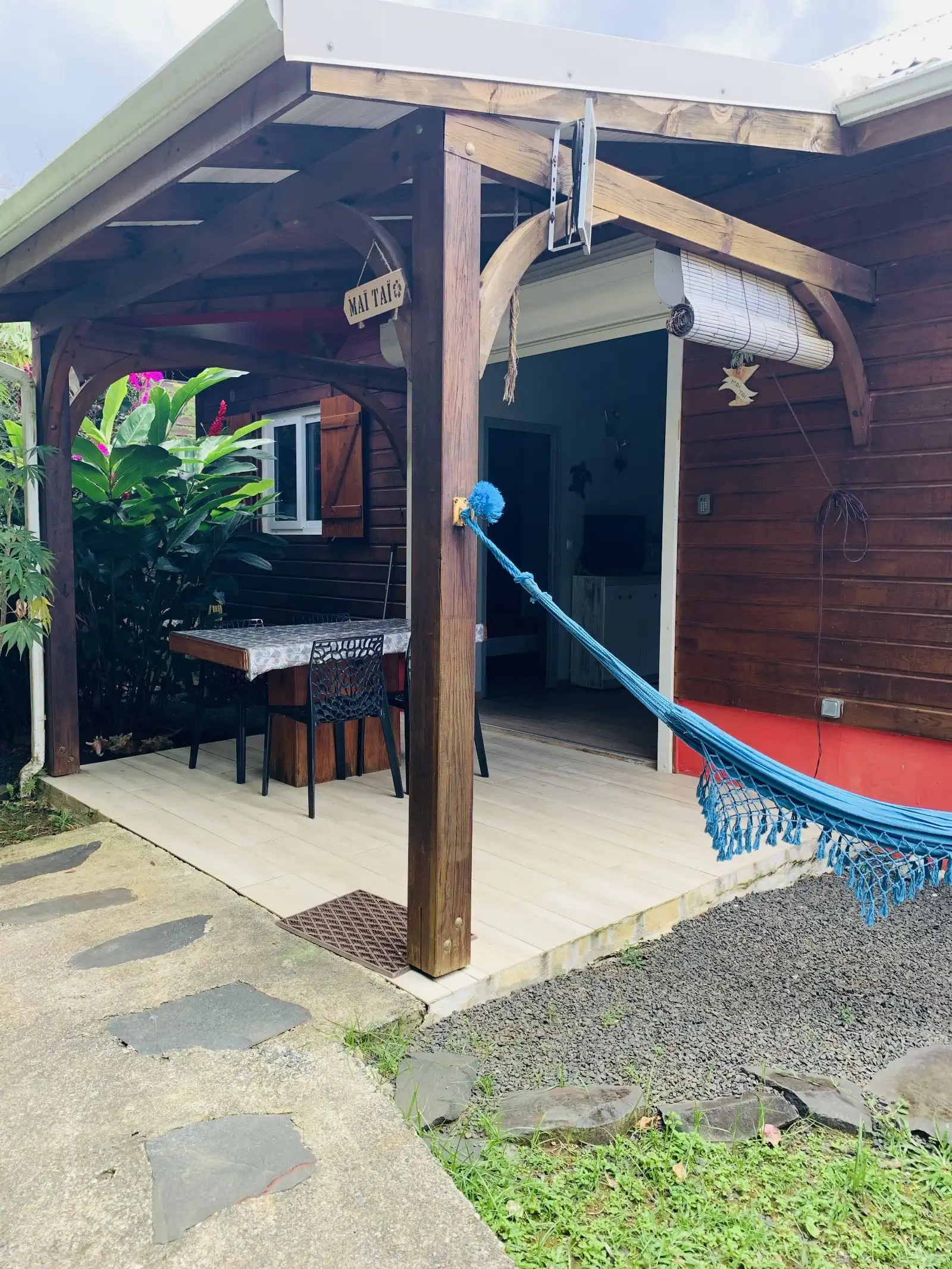 Terrasse d’un cottage avec table, chaises et hamac bleu tendu sous l’auvent