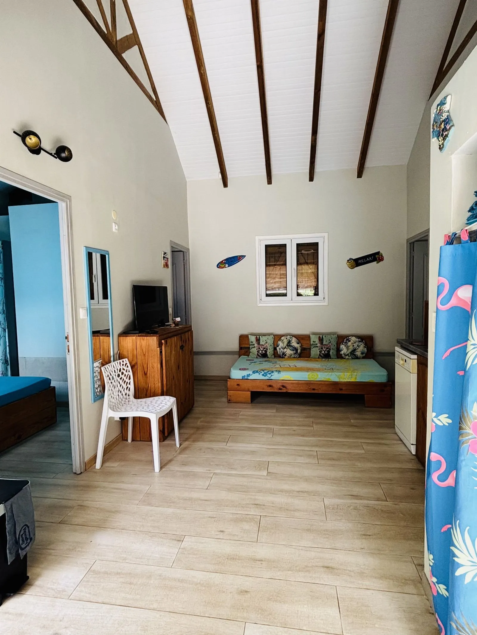 Séjour sous charpente apparente, avec banquette en bois, télévision et rideau à motif flamants roses