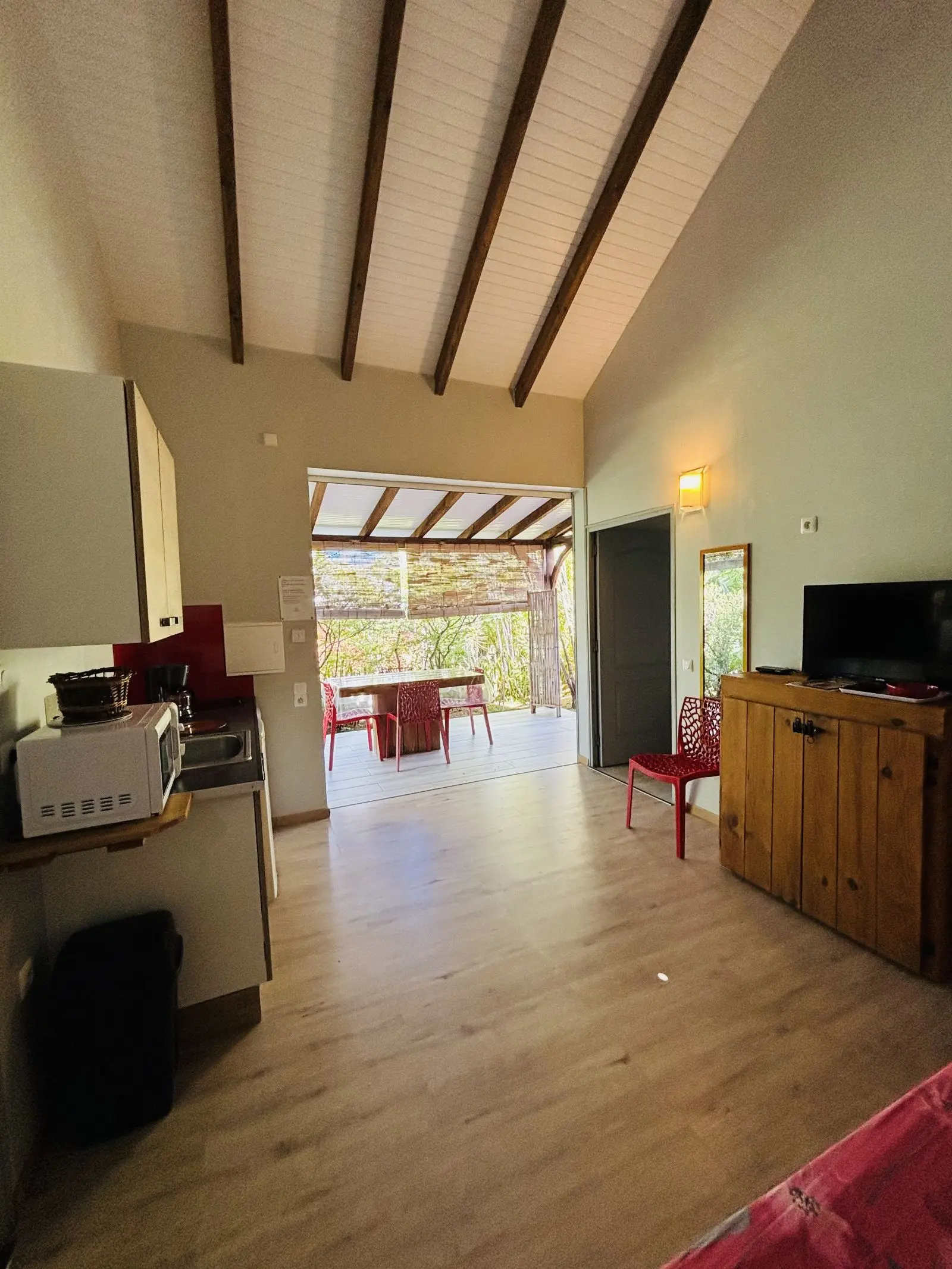 Séjour ouvert sur la terrasse et sa table, avec télévision et meuble en bois