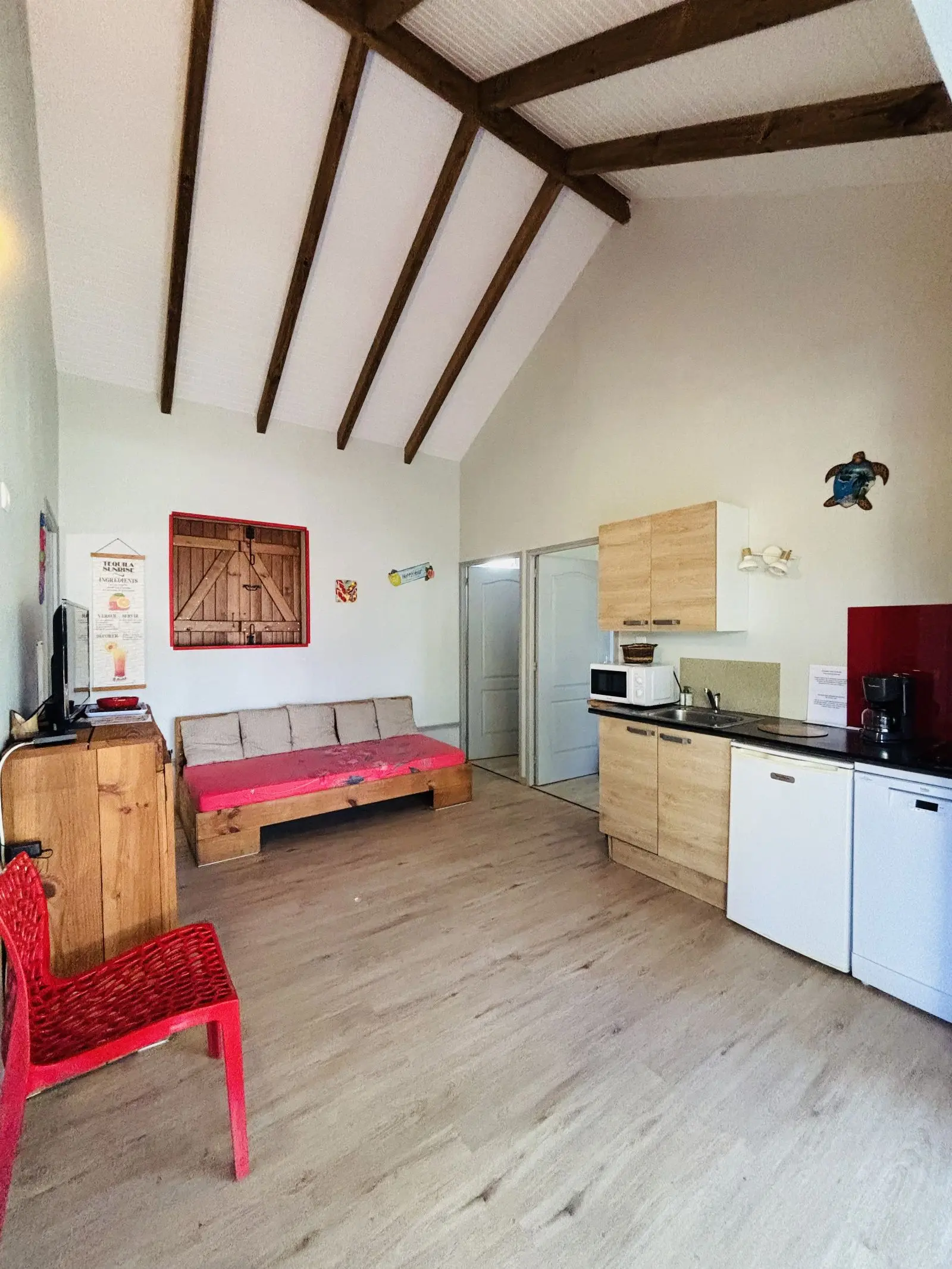Séjour avec banquette à coussins fleuris, kitchenette équipée et plafond sous charpente