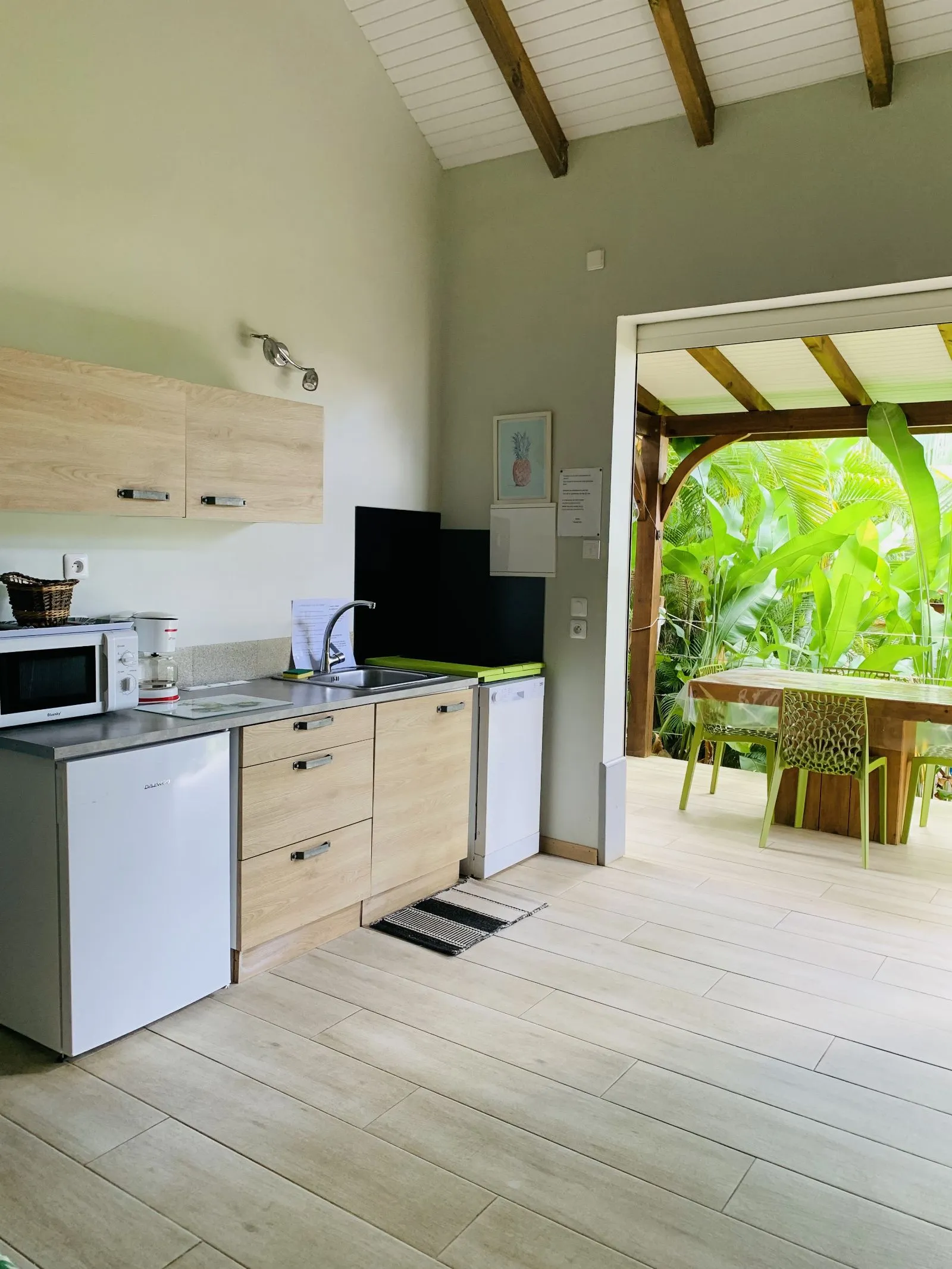 Kitchenette claire avec réfrigérateur et micro-ondes, ouverte sur la terrasse et le jardin