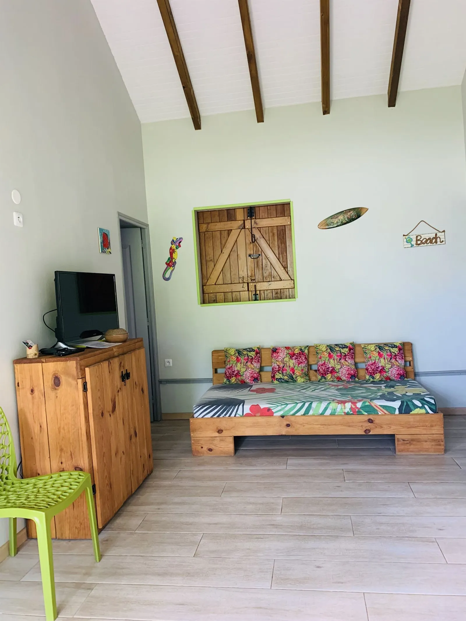 Banquette basse à coussins fleuris sous un tableau en bois, face à la télévision