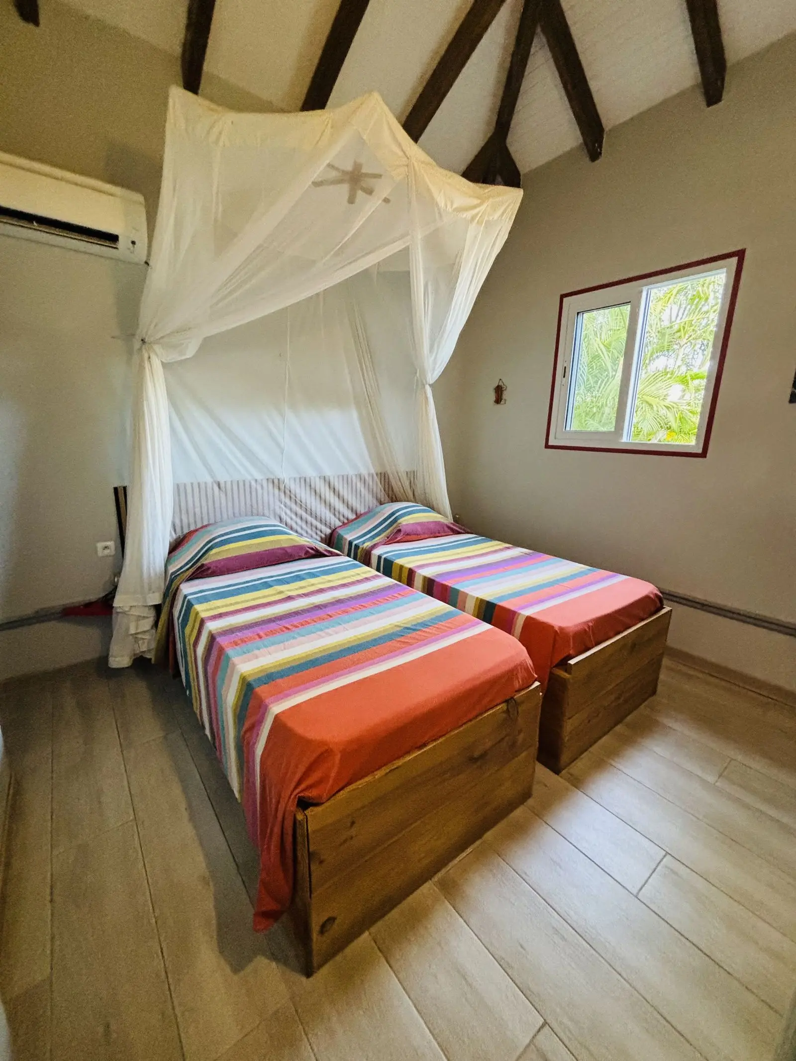 Chambre avec deux lits simples habillés de madras coloré, sous moustiquaire