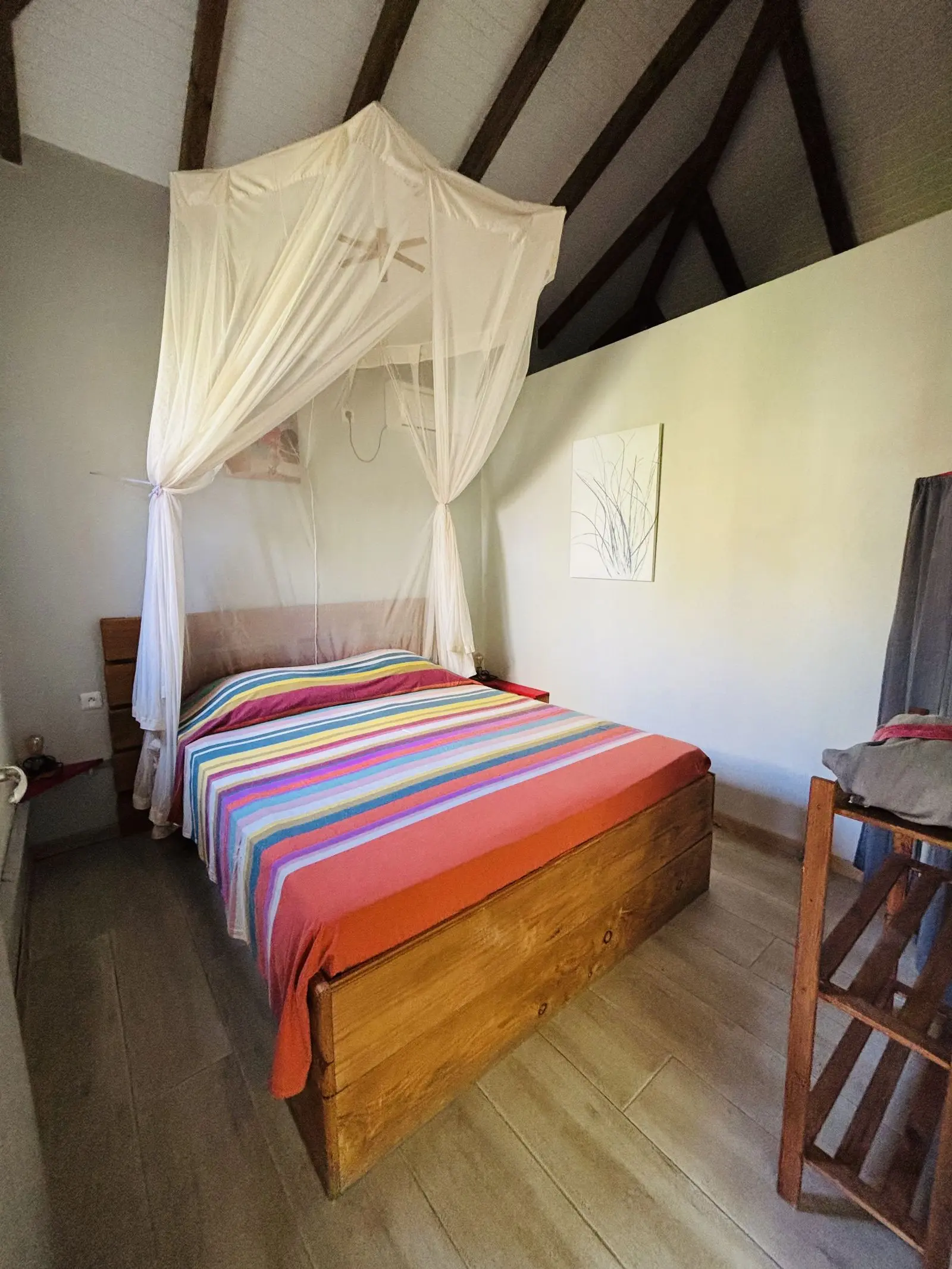 Lit double en bois sous moustiquaire, couvert d’un tissu rayé multicolore