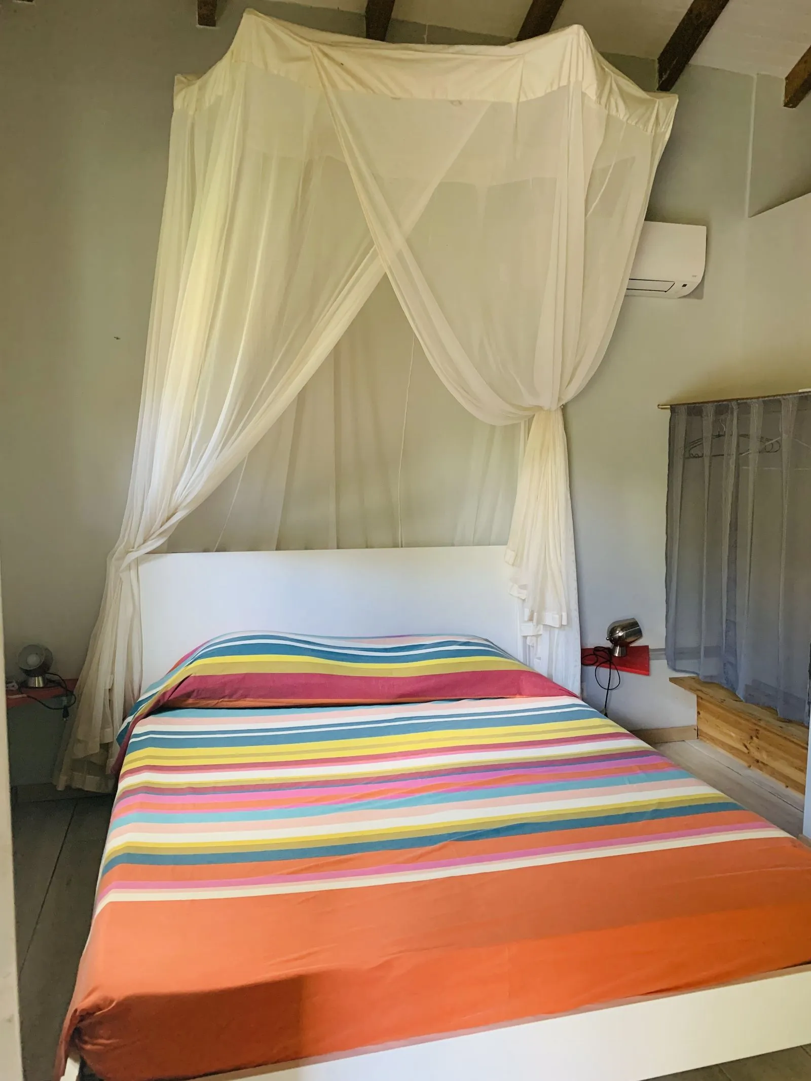 Lit double sous moustiquaire à baldaquin, avec couverture rayée et climatiseur