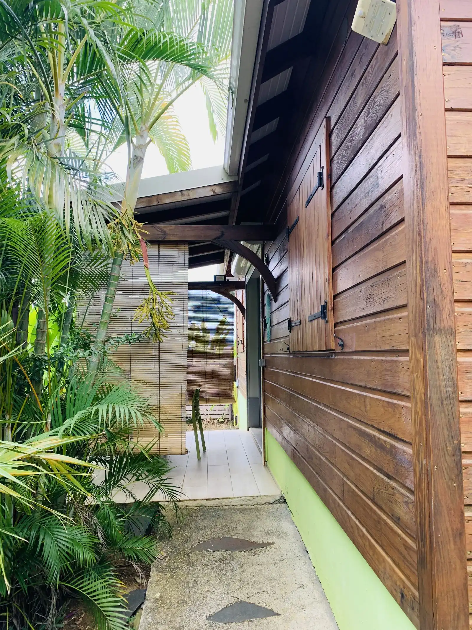 Allée dallée le long d’un cottage en bois, bordée de palmiers