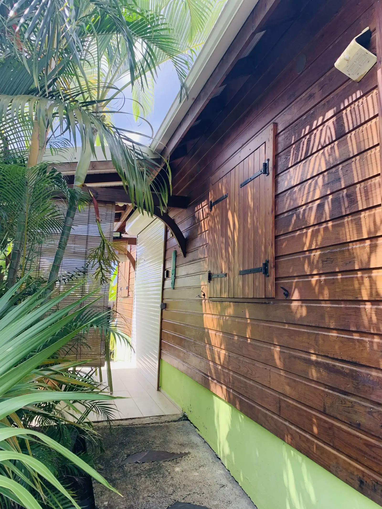 Bardage en bois d’un cottage avec ses volets, le long d’une allée plantée